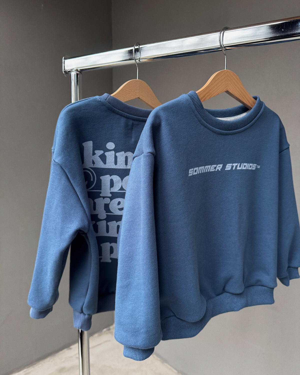 Two blue sweatshirts hanging on a rack with visible branding.