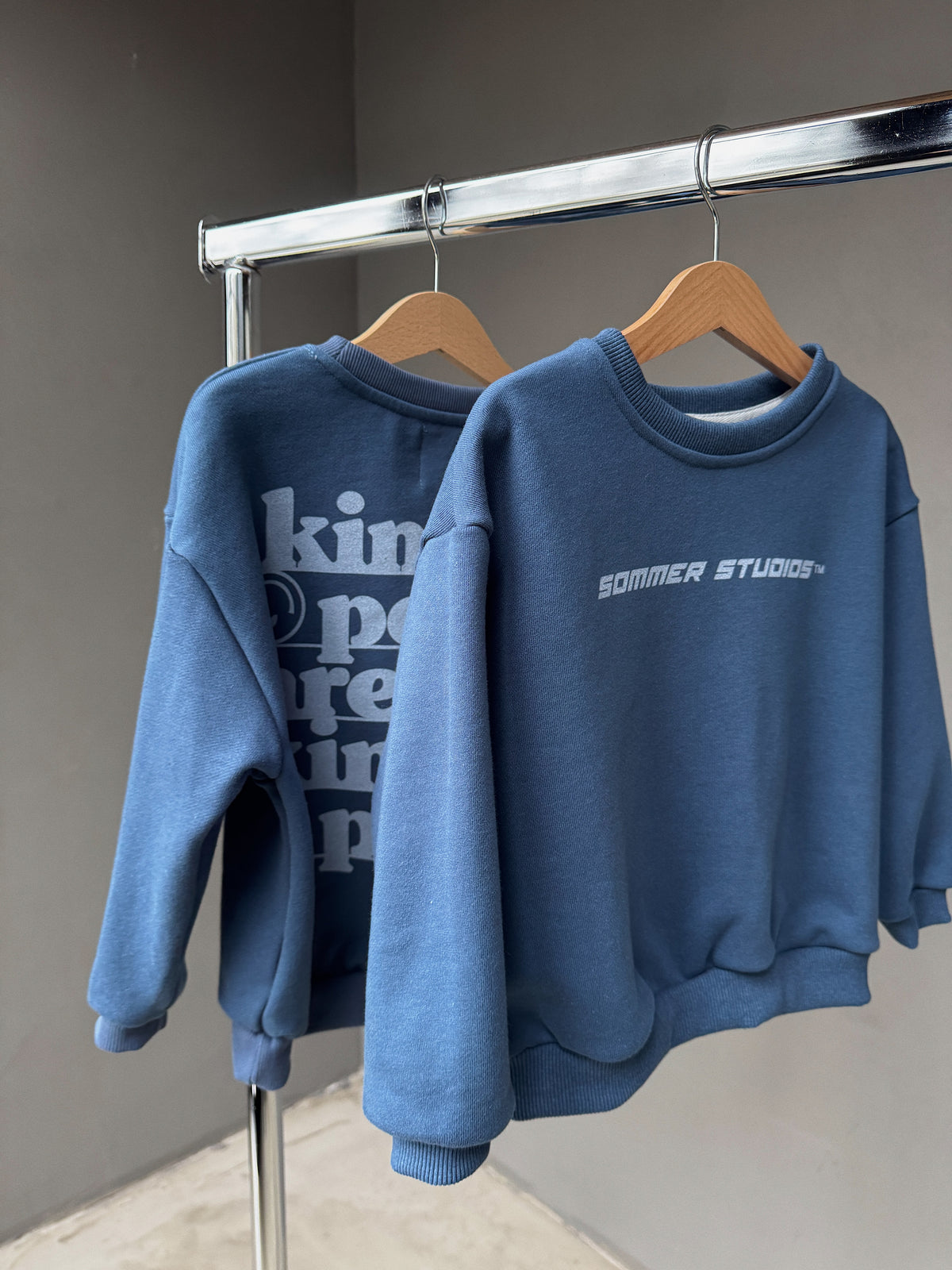 Two blue sweatshirts hanging on a rack with visible branding.